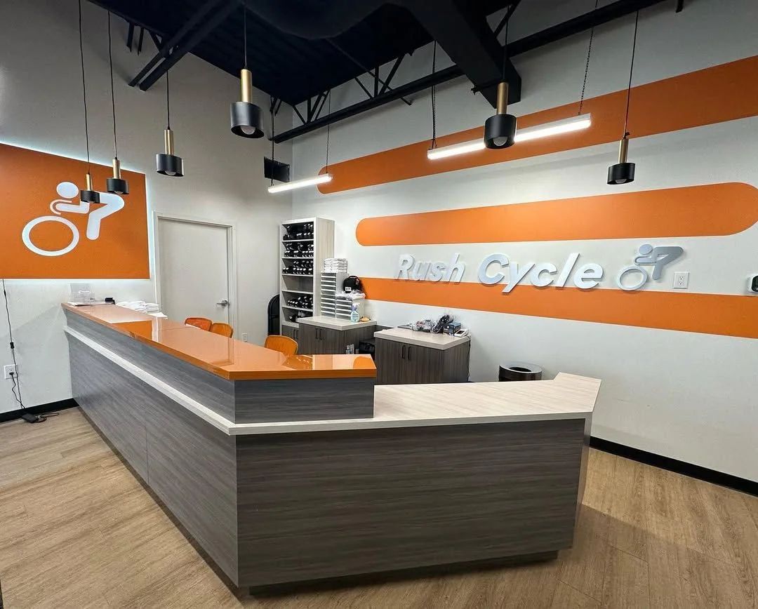 Commercial reception counter with an orange laminate top and a dark wood body in a Rush Cycle studio