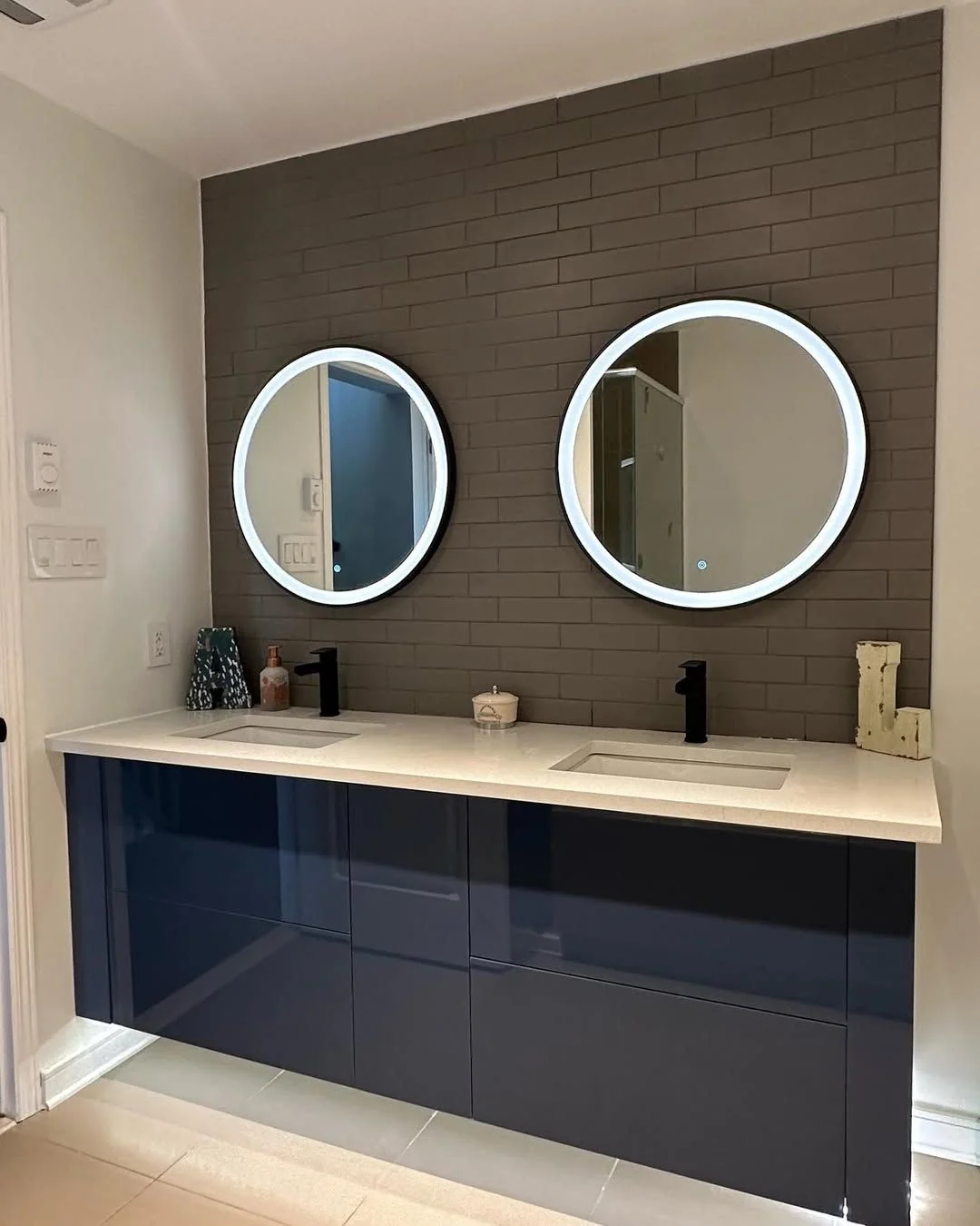 Vanité double bleu marine lustrée suspendue avec deux miroirs ronds éclairés sur un mur de brique foncée, par Limakdéco