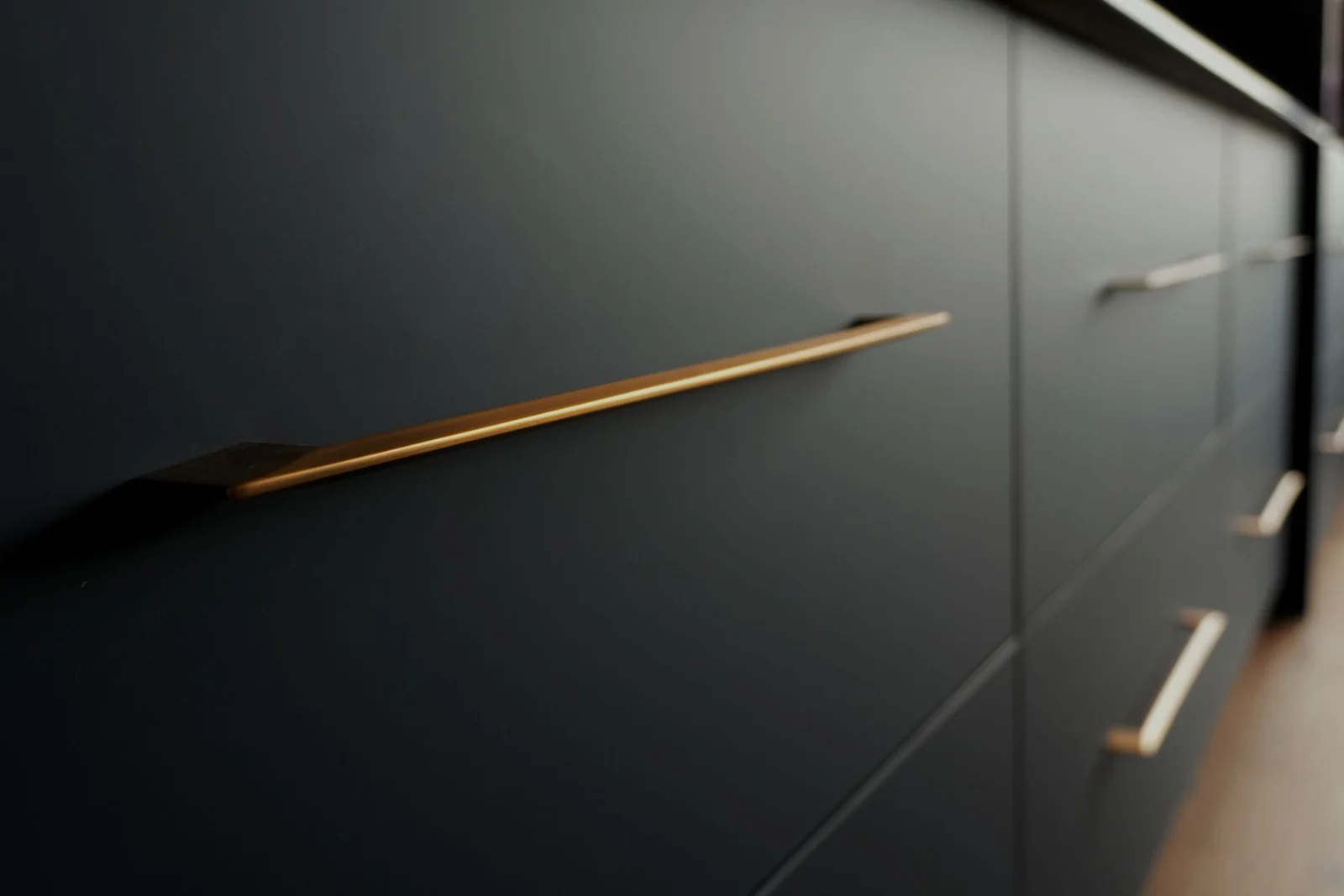 Close view of a slim brass bar pull mounted on a dark cabinet door, by Limakdeco