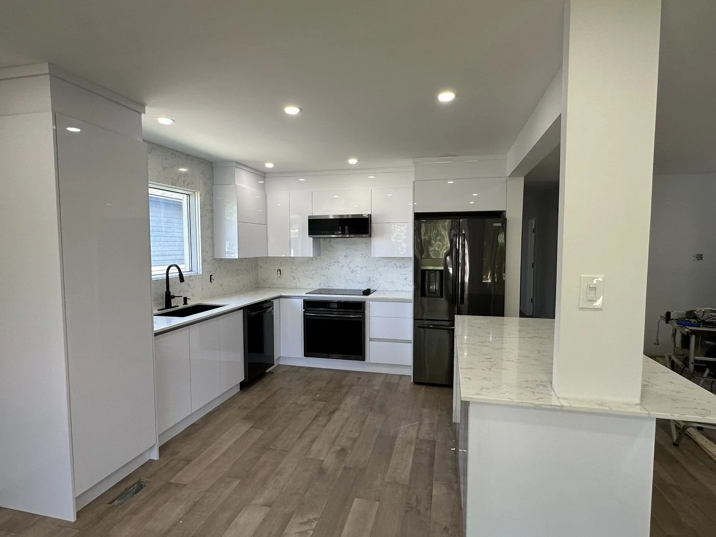White kitchen with black appliances, quartz countertops and an open plan dining area beyond, Montreal