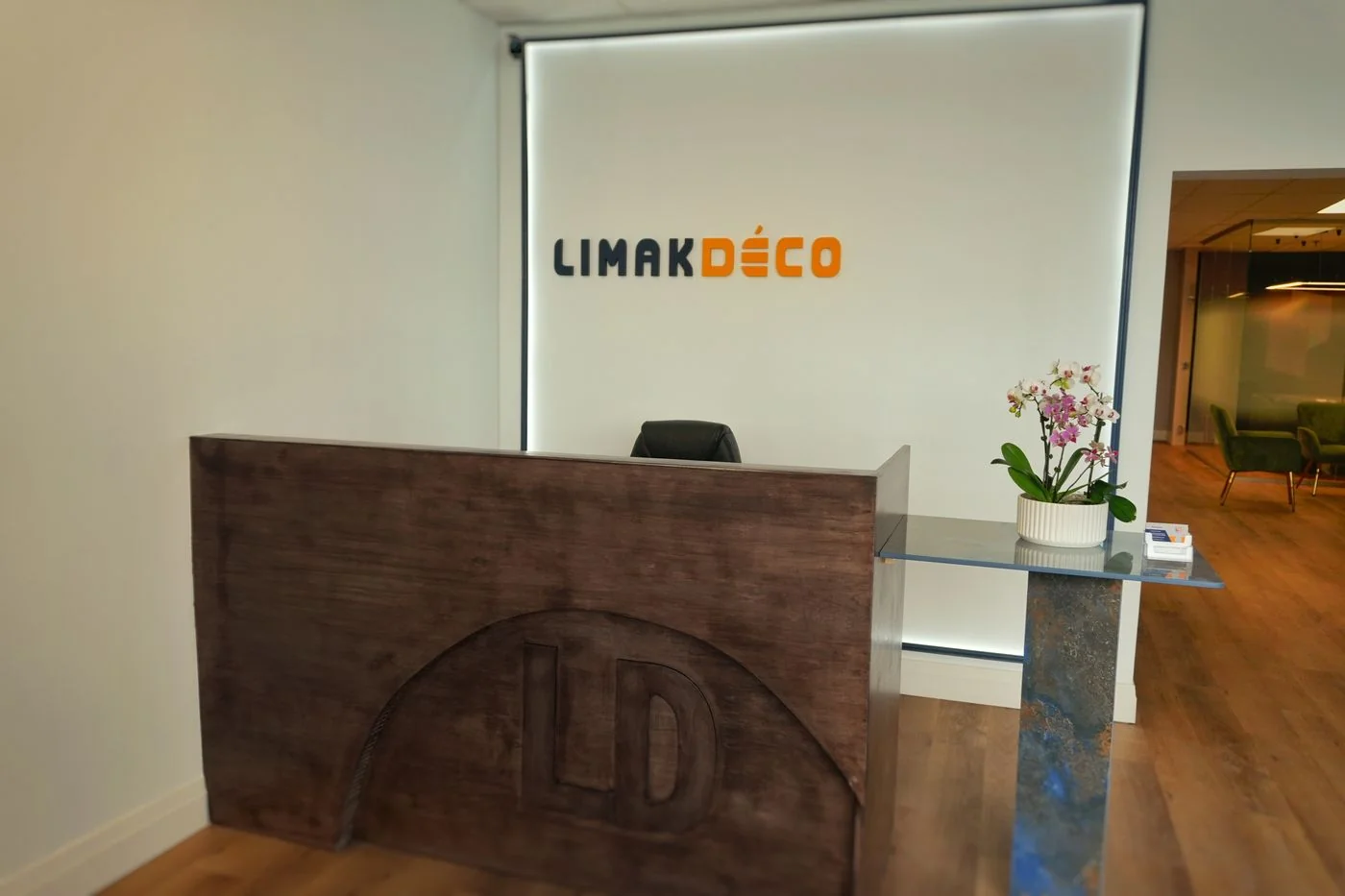 Comptoir d’accueil en bois avec panneau au logo embossé devant une enseigne Limakdéco rétroclairée, avec une aire d’attente au fond