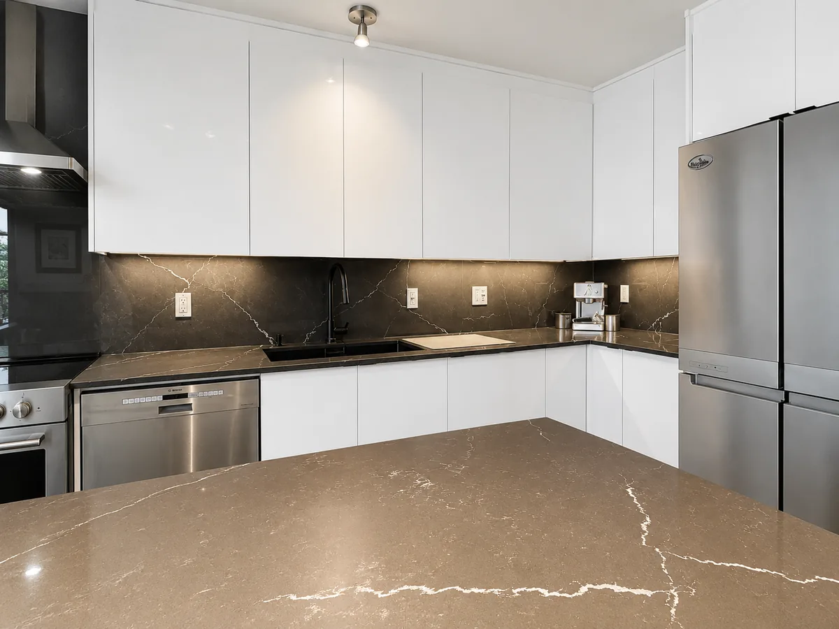 Quartz noir au veinage blanc sur l'îlot et dosseret pleine hauteur d'une cuisine blanche sans poignées à Pierrefonds