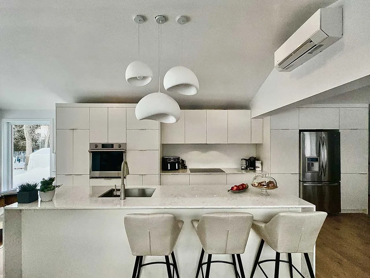 Mur de cuisine blanc mat aux lignes de portes alignées et suspensions blanches sculpturales au-dessus de l'îlot, Laval
