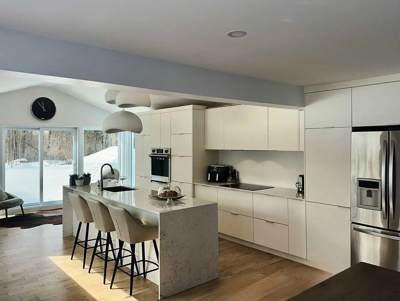 Cuisine sur mesure blanc mat avec îlot en quartz à double cascade et suspensions sculpturales dans une construction neuve à Laval