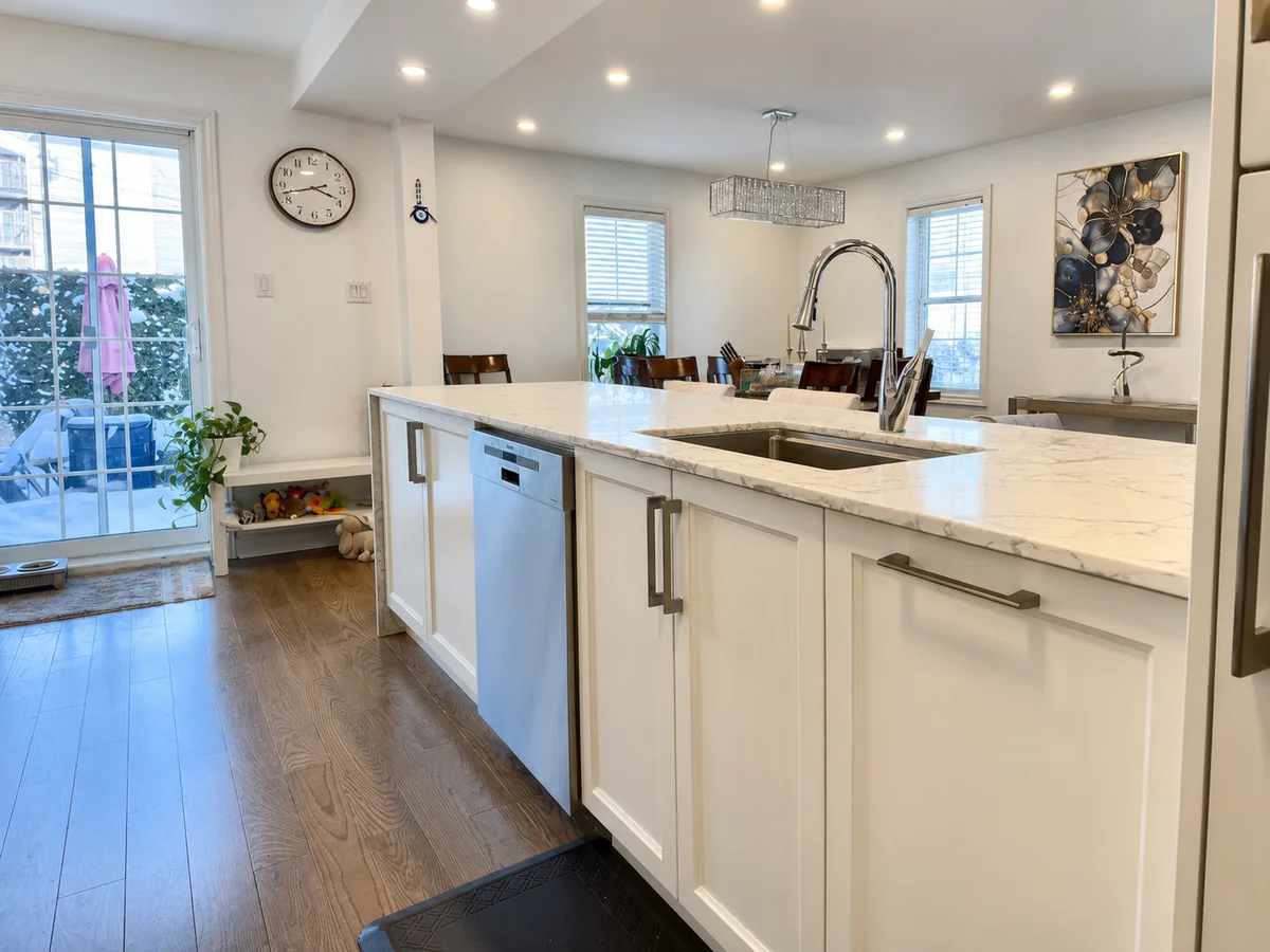 Nine foot white island with quartz top and integrated dishwasher in a renovated Bois-Franc kitchen, dining area beyond