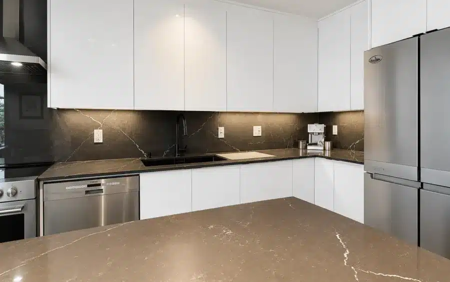 Black quartz island and full-height backsplash with white handleless cabinets in a Limakdéco kitchen in Pierrefonds